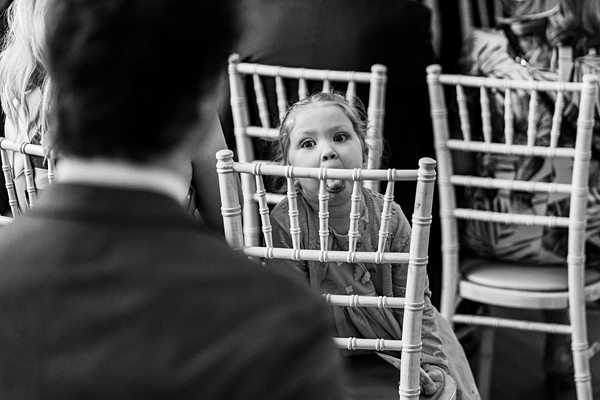 Child peeking through chairs at event in black and white.