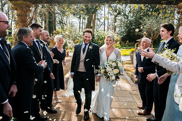 Joyful wedding couple walking, guests throwing petals.