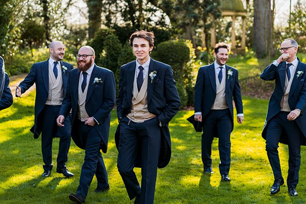 Groom and groomsmen smiling in garden.