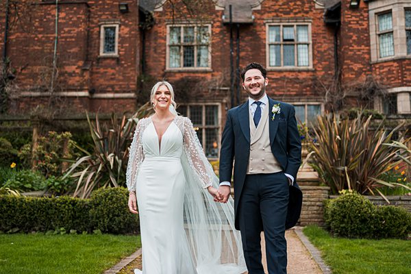 Bride and groom walking by manor garden.