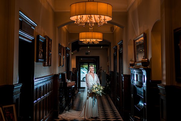 Bride standing in elegant hallway with chandelier.