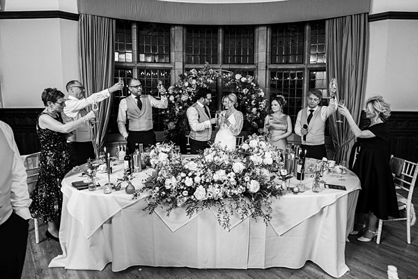 Wedding guests toasting at reception table with floral arrangement.