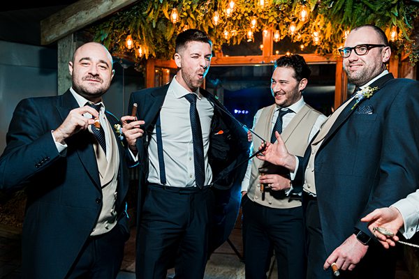 Groomsmen celebrating with cigars at evening wedding reception.