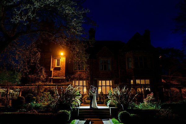 Couple embracing at night outside illuminated house.