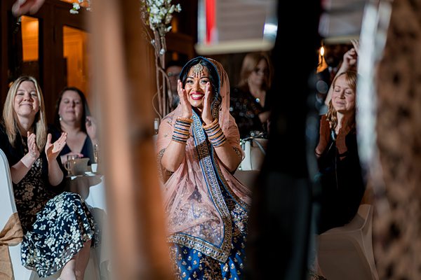 Bride in traditional attire smiling at wedding celebration.
