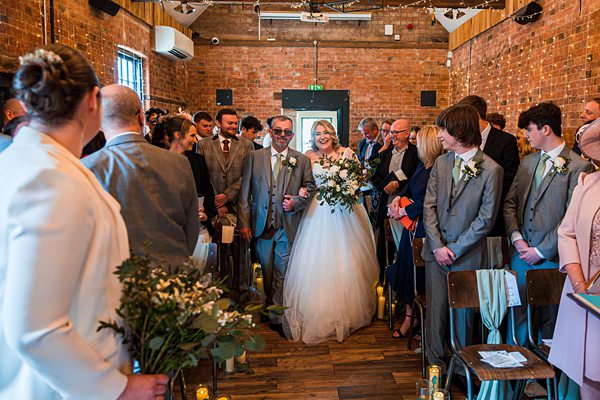 Bride walking down aisle at rustic wedding venue.