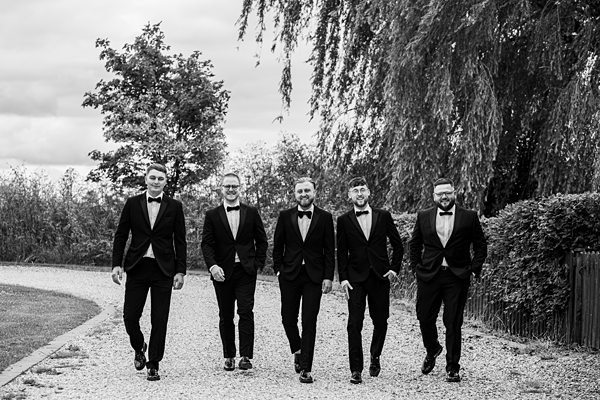 Groomsmen walking in tuxedos at outdoor wedding.