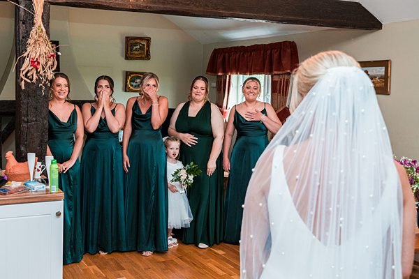 Bridesmaids in green dresses emotional at wedding ceremony.