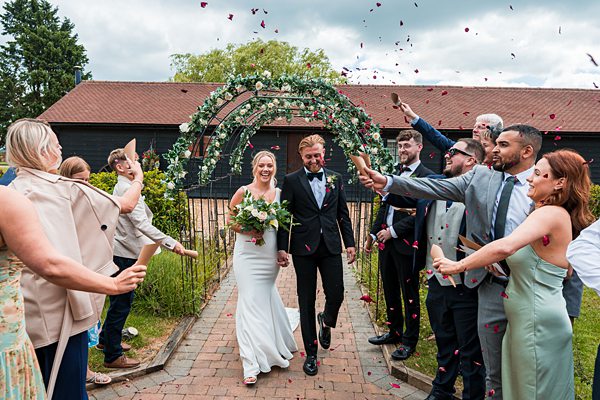 Newlyweds exiting ceremony under flower arch with confetti.