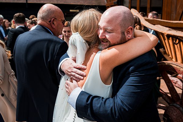 Emotional wedding hug with guests in background.