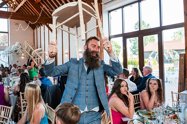 Man in suit holding chair aloft at wedding reception.