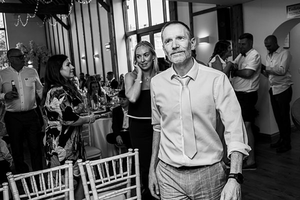 Man walking at wedding reception, guests in background.
