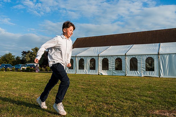 Boy running on grass near marquee tent.