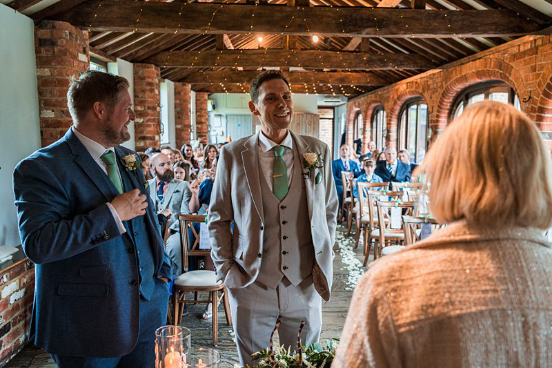 Groom smiling during wedding ceremony in rustic venue.