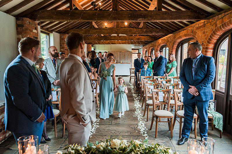 Bride walking down aisle at rustic wedding ceremony.