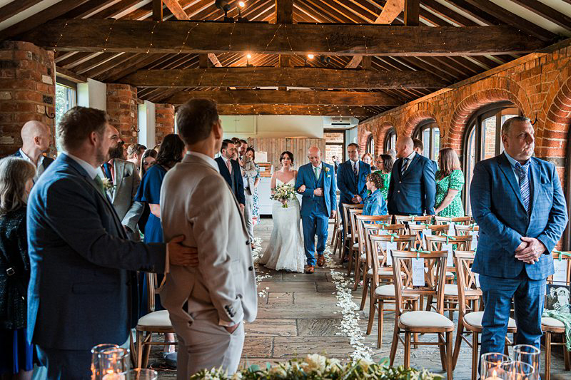 Bride walking down aisle at rustic wedding venue.