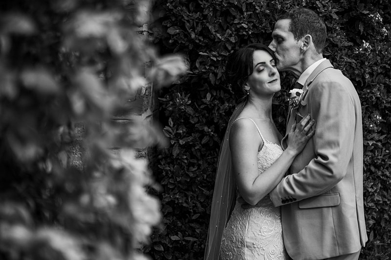 Bride and groom kissing, leafy background, black and white photo.