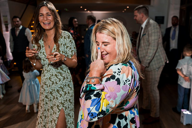 Women laughing at festive event with guests in background.