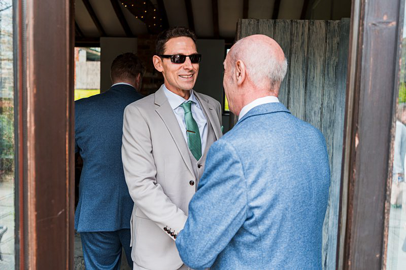 Smiling men in suits greeting at event entrance.