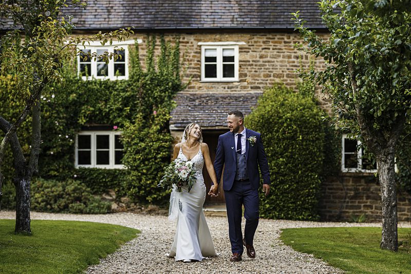 Bride and groom walking by countryside house.