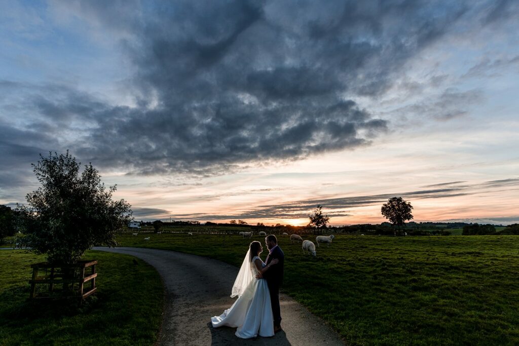 Couple embracing at sunset in countryside wedding scene.