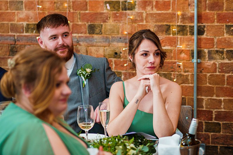 Guests at wedding reception with exposed brick backdrop.