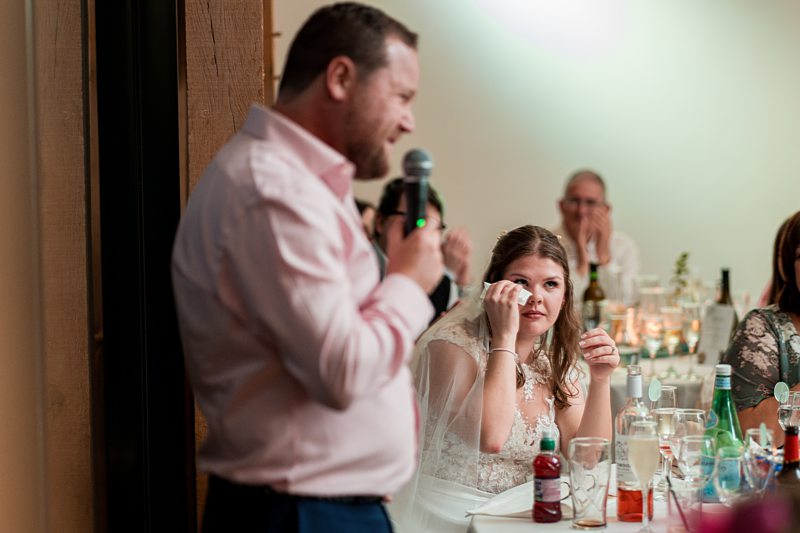 Man speaking into microphone at wedding, bride listening attentively.