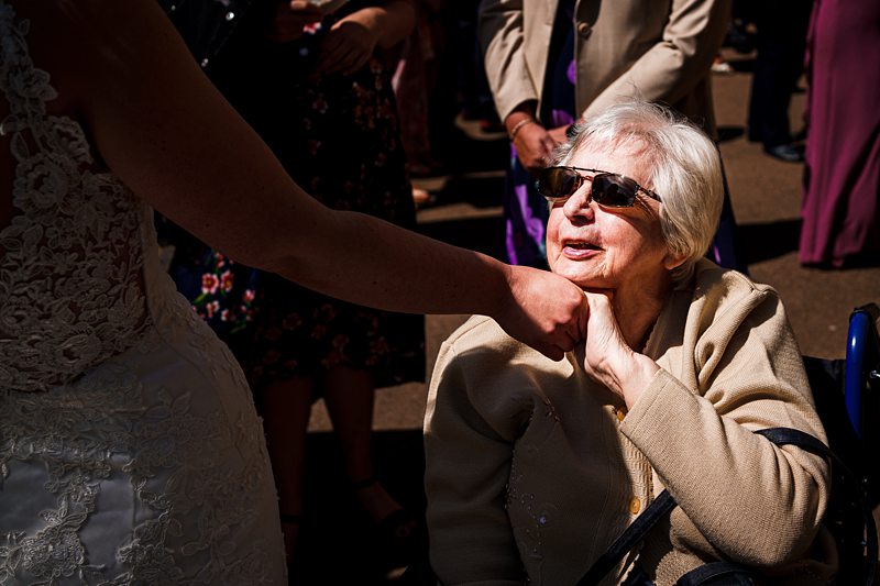 Elderly lady in sunglasses at sunny wedding event.