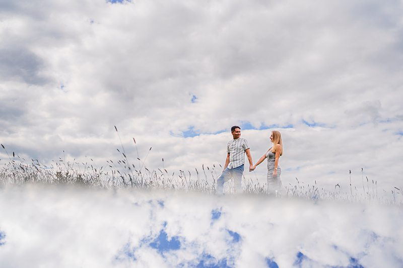 Couple holding hands in field under cloudy sky