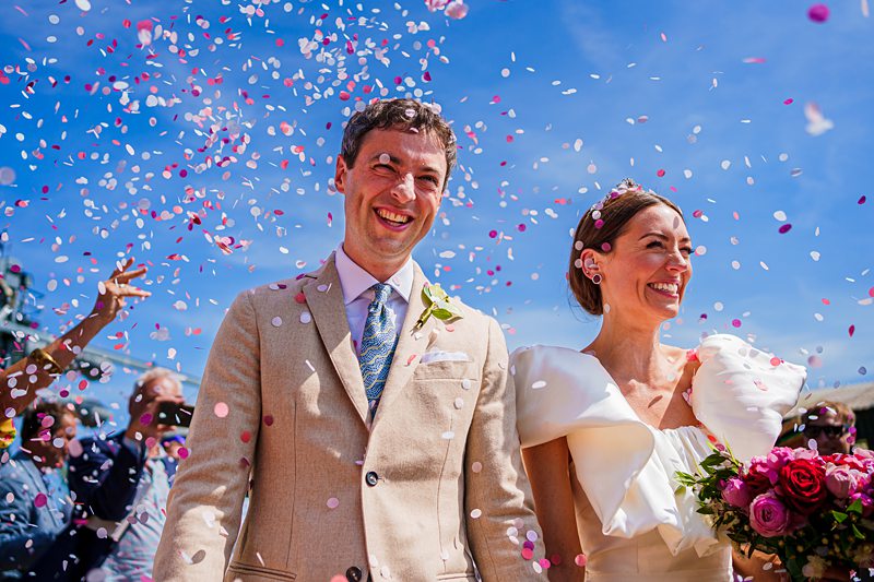 Joyful wedding couple with confetti and blue sky.