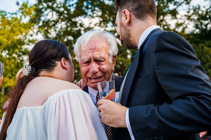 Elderly man emotional at wedding with family.