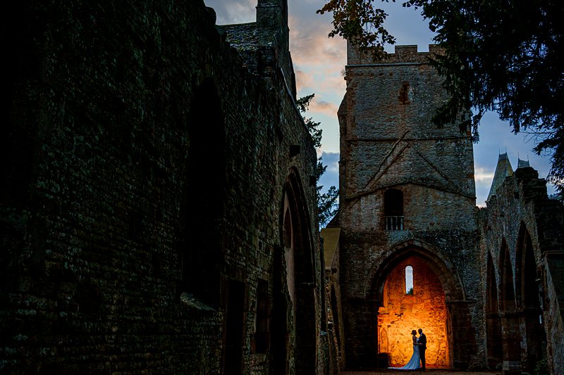 Couple silhouetted in illuminated historic castle ruins at dusk.