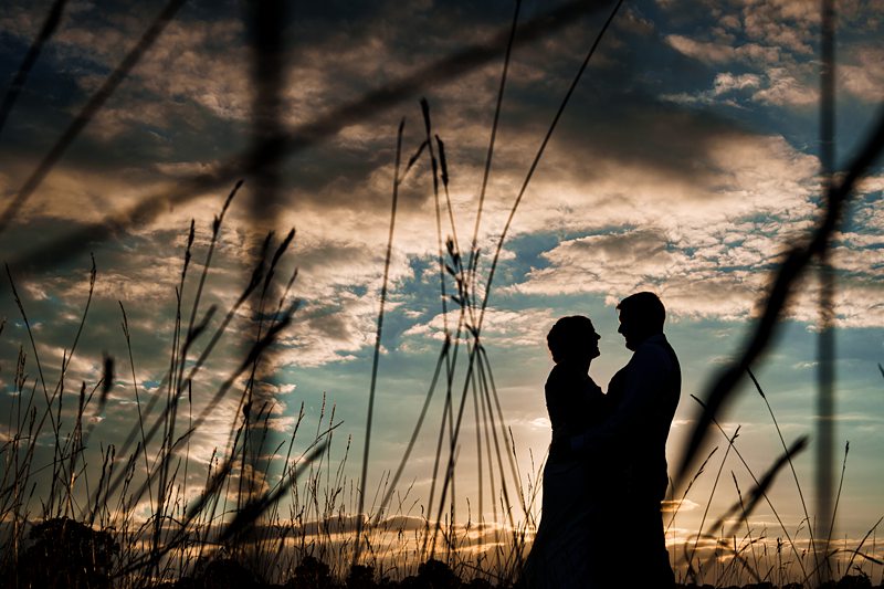Silhouetted couple at sunset in grassy field.