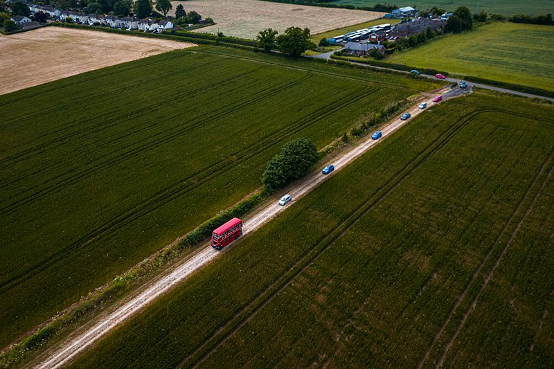 Aerial view of cars on rural road through green fields.
