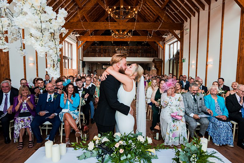 Couple kissing at wedding ceremony with guests watching.