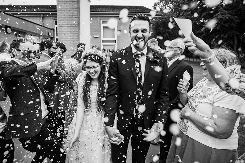 Joyful wedding confetti celebration with smiling couple.