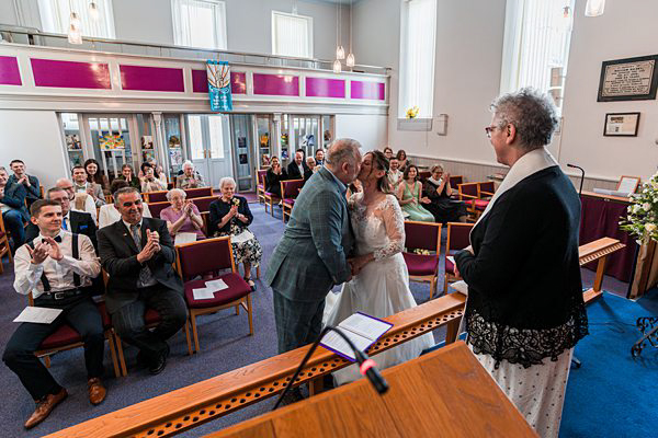 Couple kissing in wedding ceremony with guests applauding.