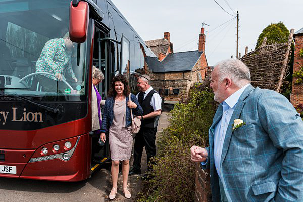 People disembarking from red bus in village setting.