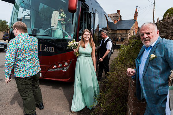 Wedding guests alighting from bus in countryside setting.