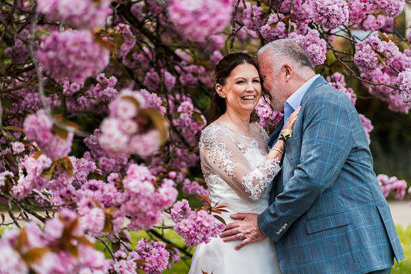 Couple embracing amidst blooming pink cherry blossoms.