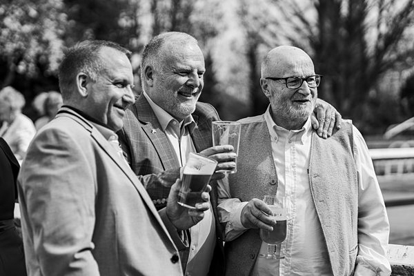 Three men smiling and holding drinks at outdoor event.