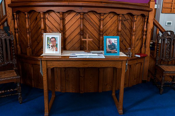 Alt: Wooden church altar with two framed photographs.