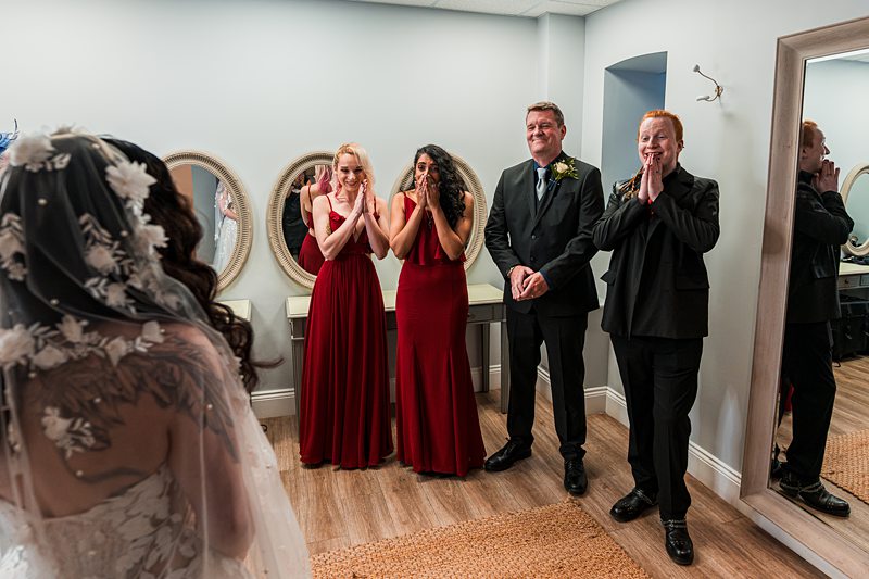 Bridal party reacting to bride in preparation room.