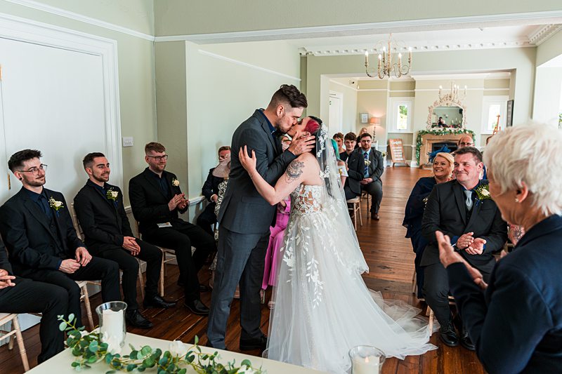Bride and groom kiss at wedding ceremony with guests.