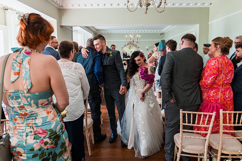 Bride and groom walk down the aisle, smiling guests.