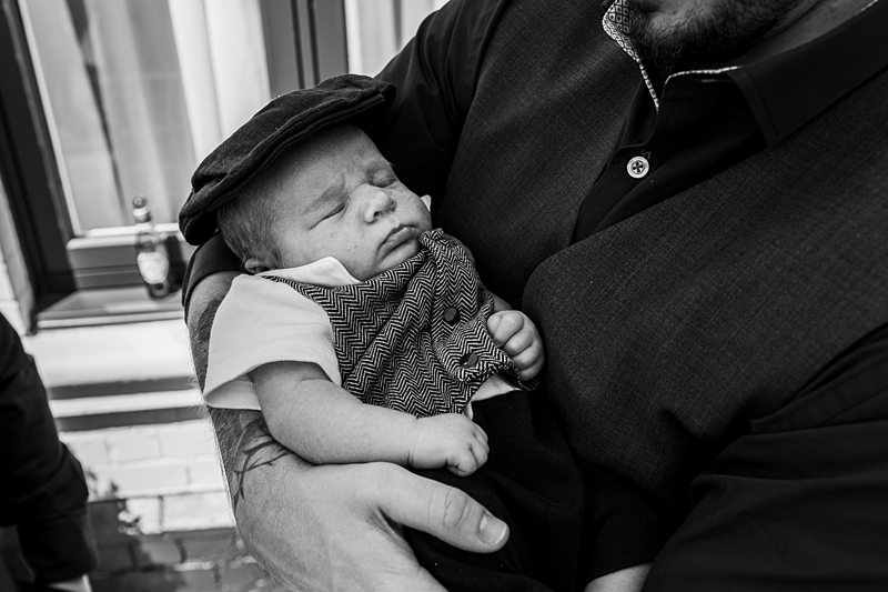 Baby sleeping in arms, wearing cap and vest.