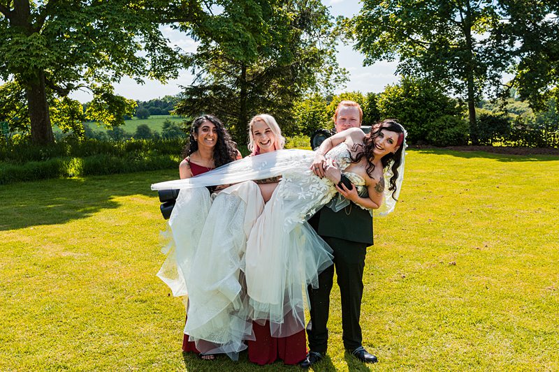 Group lifting bride on sunny wedding day.
