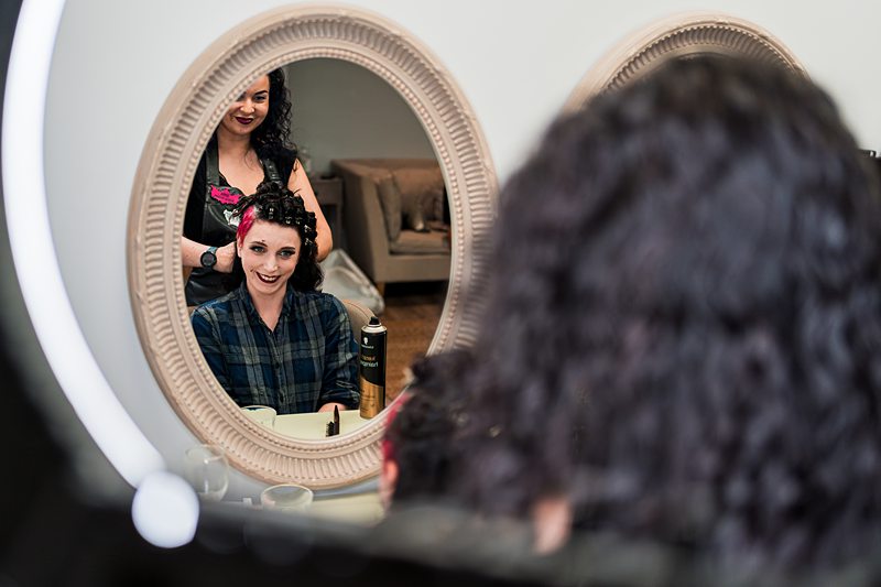 Woman getting curls done at salon, stylist in background.