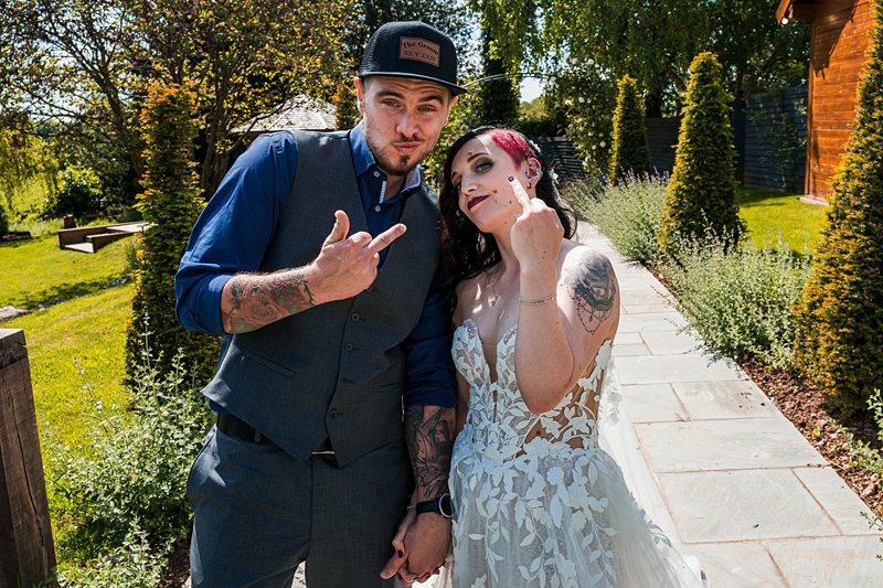 Bride and groom posing outdoors, showing middle fingers.