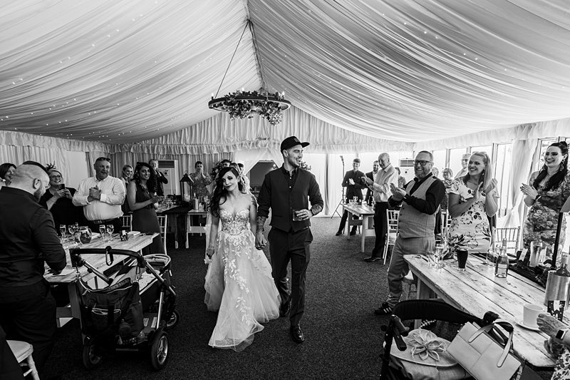 Bride and groom entering wedding reception, guests applauding.